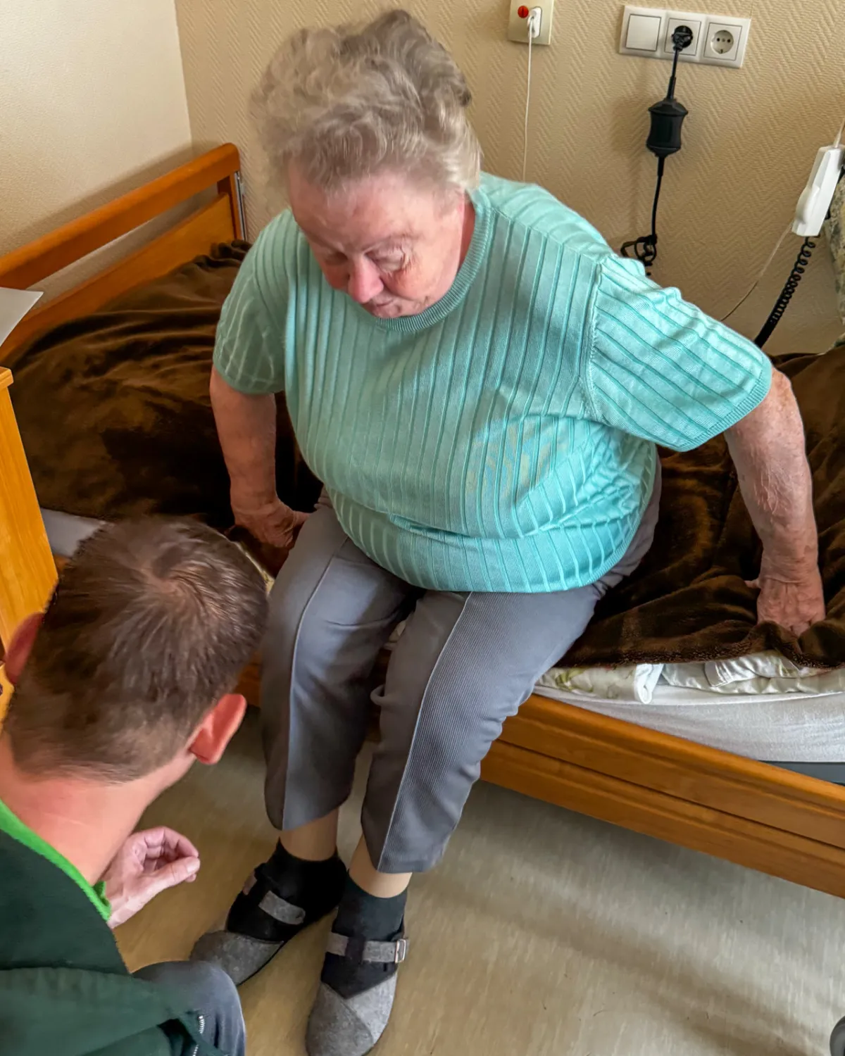 Therapeut übt mit einer Bewohnerin das Aufstehen von der Bettkante, in ihrem Zimmer
