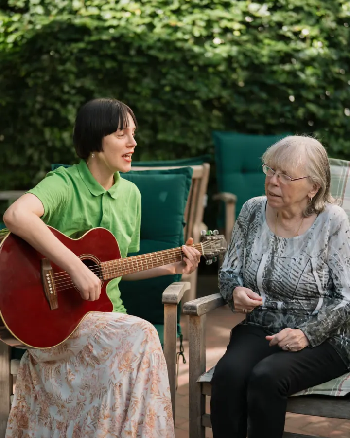 Musik im Garten: eine Therapeutin spielt Gitarre für eine Bewohnerin